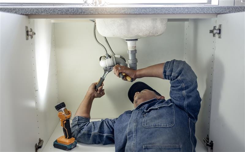 Plumber repairing pipes beneath a bathroom sink in West Sacramento
